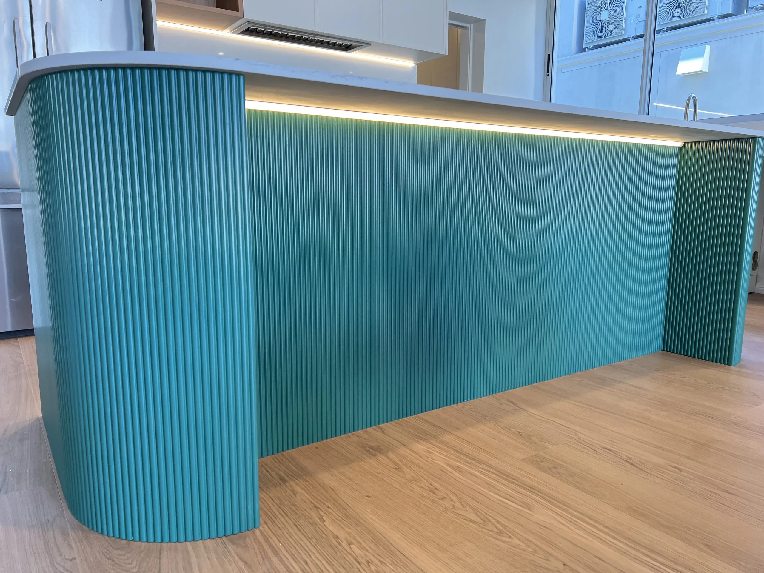 Curved kitchen island with fluted teal panels and an LED strip under the benchtop