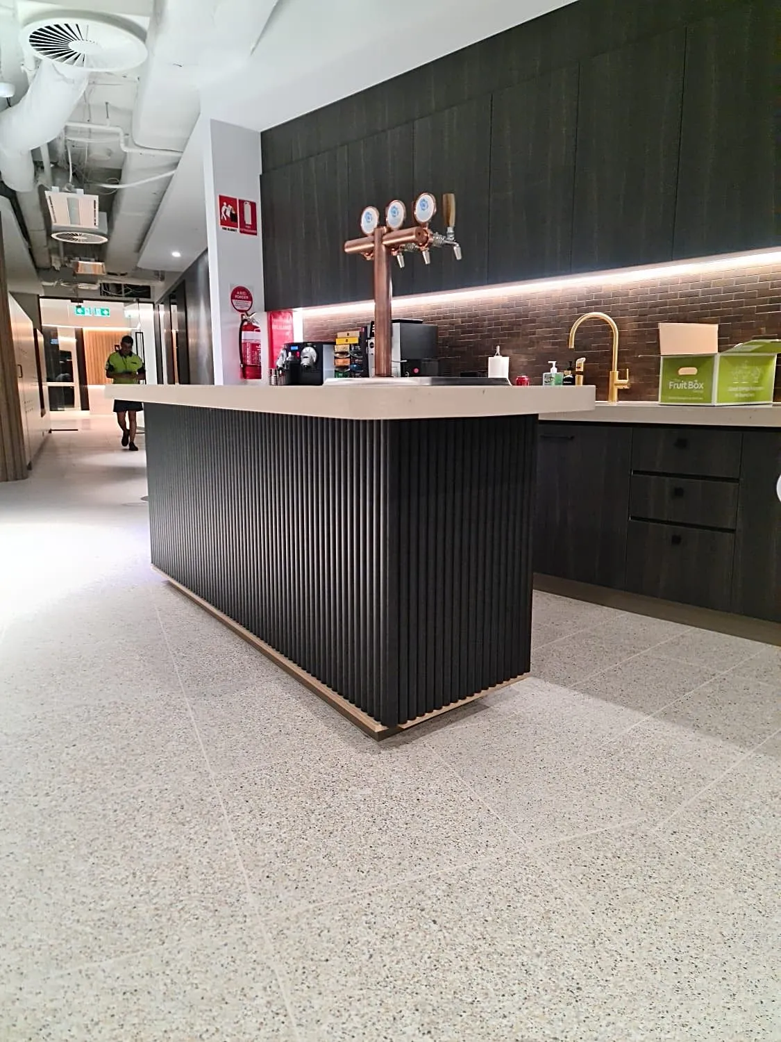 Bar counter with a dark fluted front, brass taps and an LED-lit shelf in a corporate fit-out, Sydney