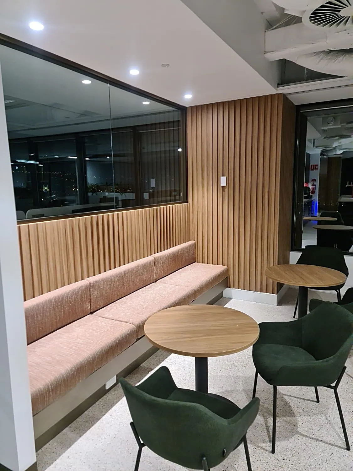 Timber-slatted wall with built-in booth seating, round tables and green chairs in a corporate fit-out, Sydney