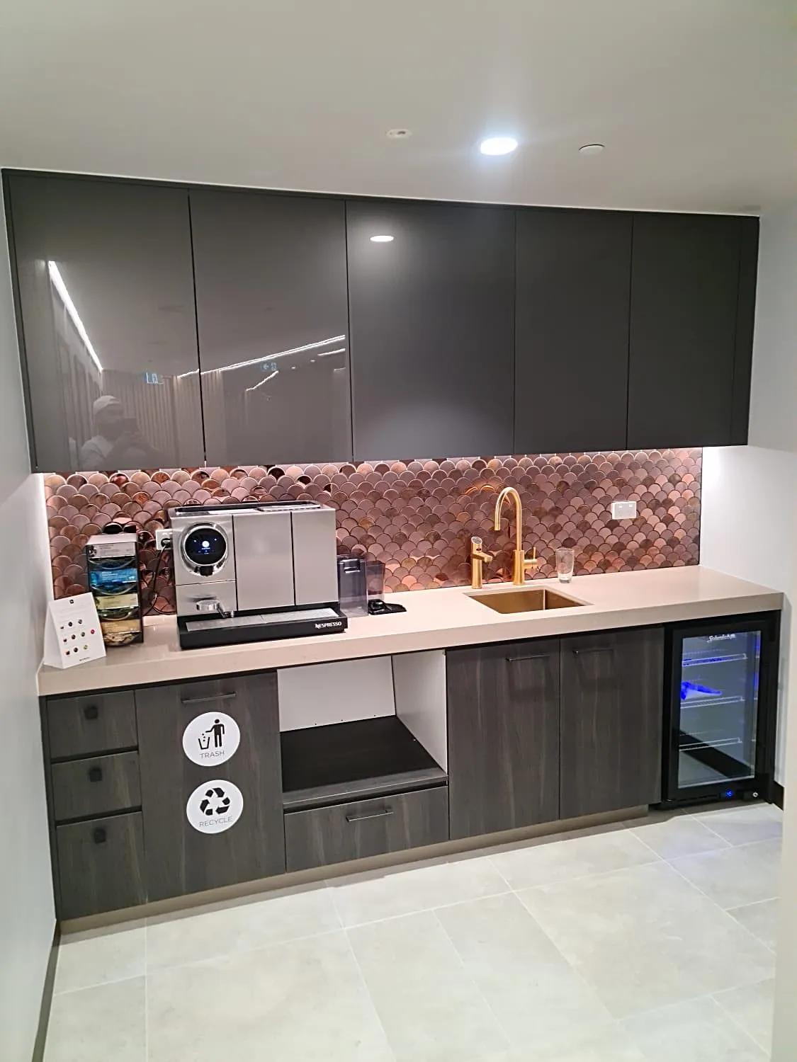 Staff kitchenette with dark cabinetry, a copper fishscale splashback, brass tap and stone benchtop, Sydney