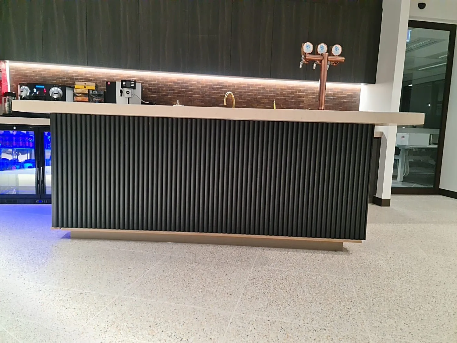 Fluted-front bar counter with a stone top and LED-lit shelf in a corporate fit-out, Sydney