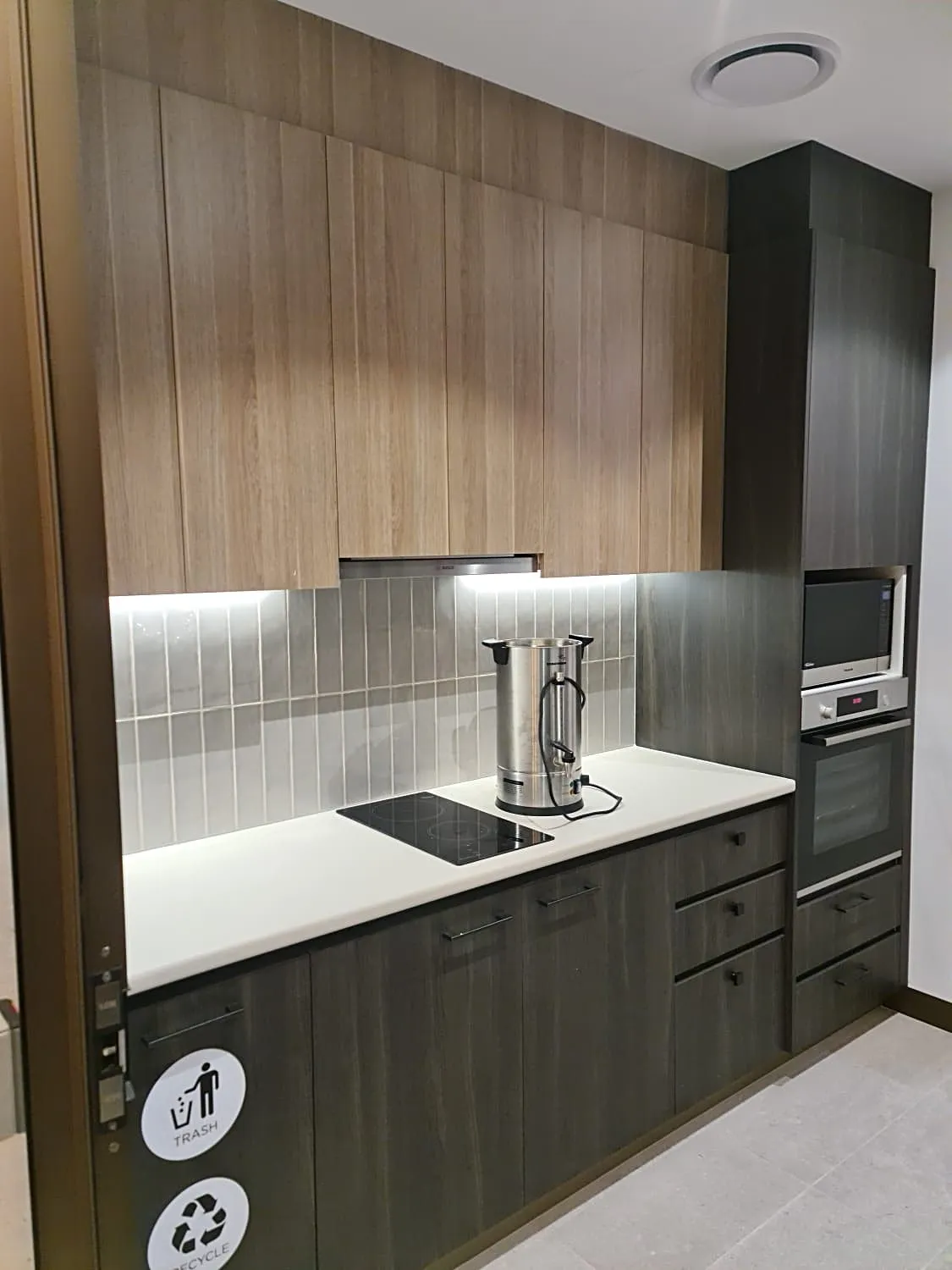Kitchenette with timber overhead cabinets, dark base cabinets, tiled splashback and integrated appliances, Sydney