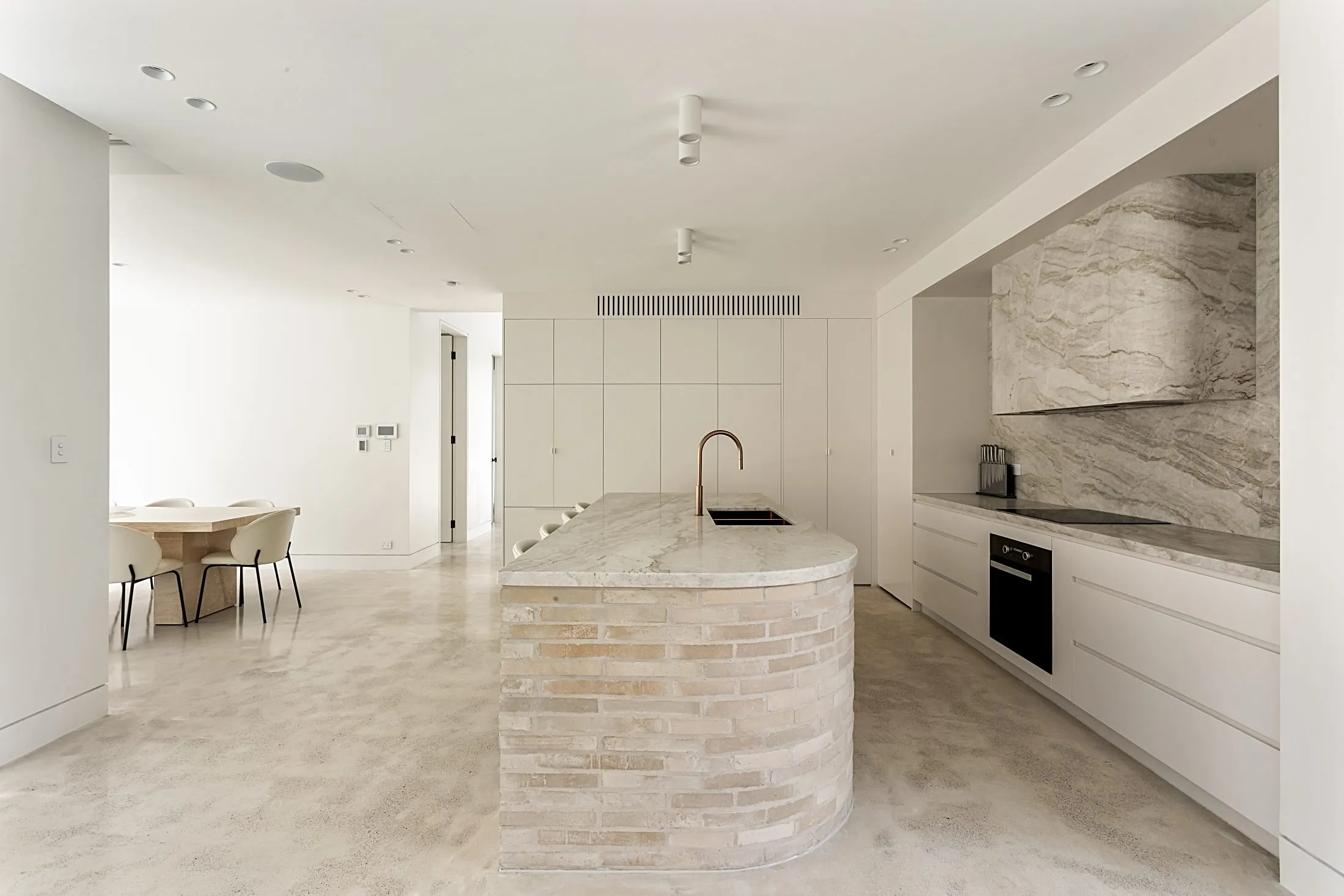 Kitchen with a curved brick-clad island, stone splashback and white cabinetry, Lilyfield