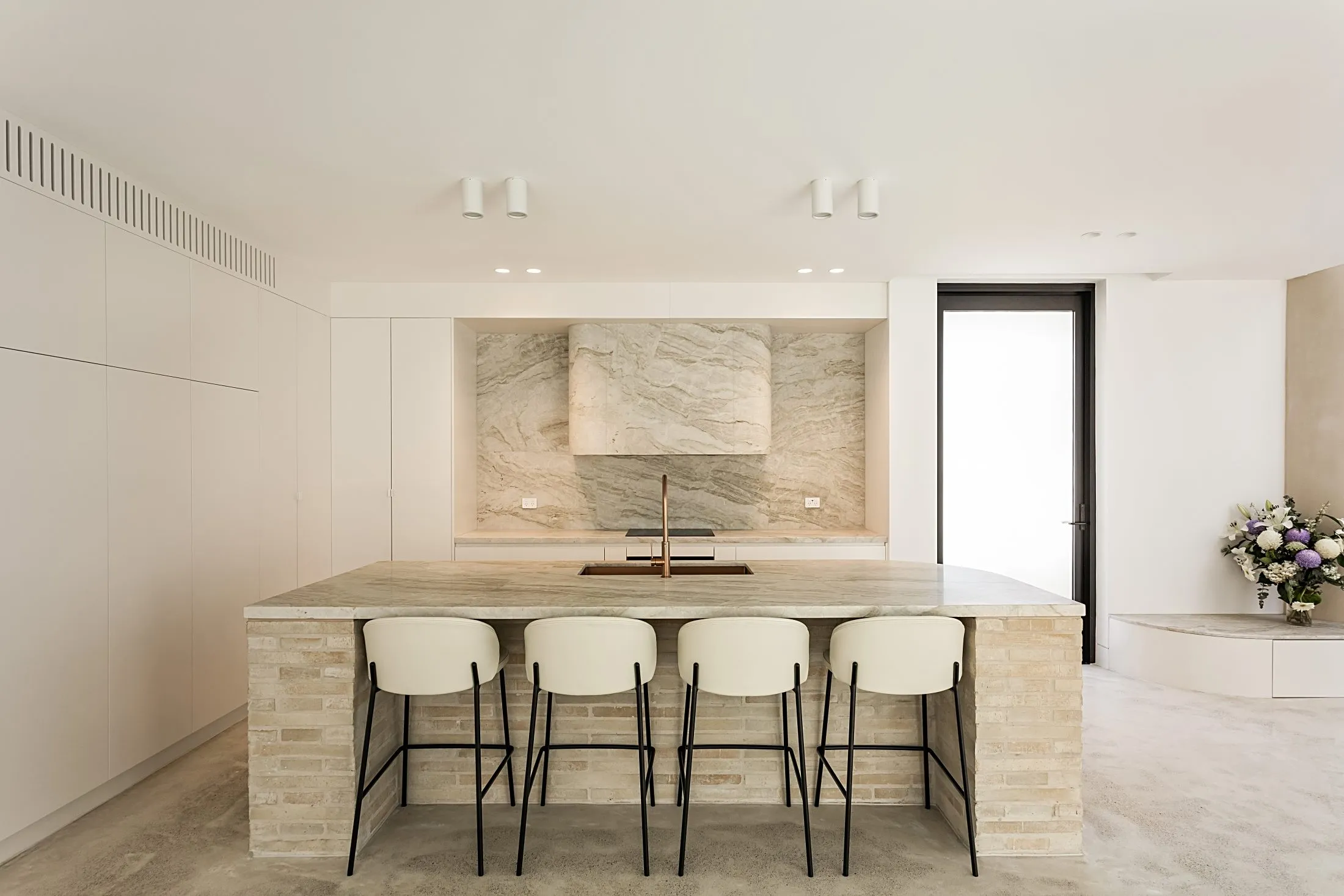 Kitchen island with a stone top, brick base and bar stools in front of a stone splashback, Lilyfield
