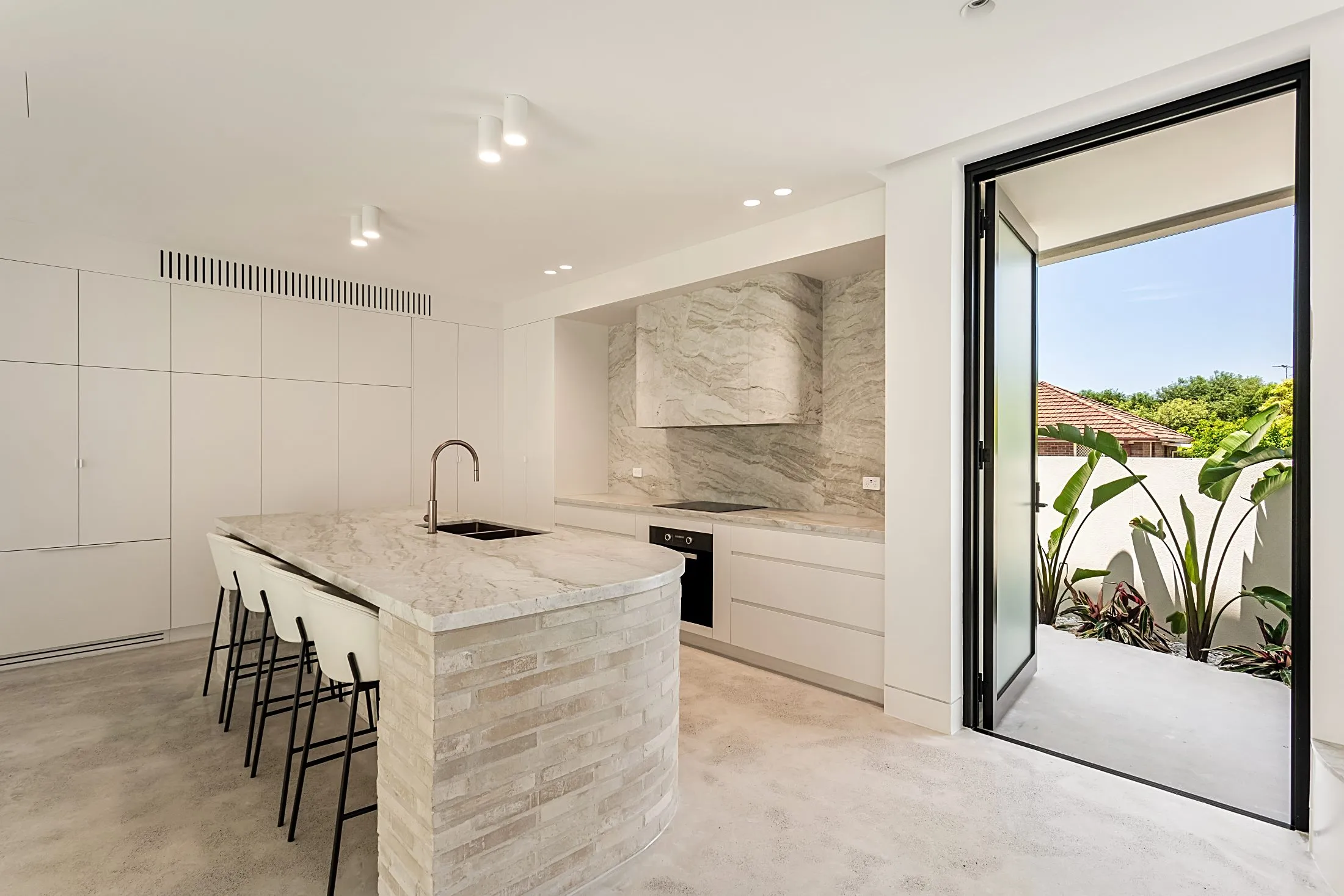 Kitchen with a curved brick island, concealed cabinetry and a courtyard door, Lilyfield