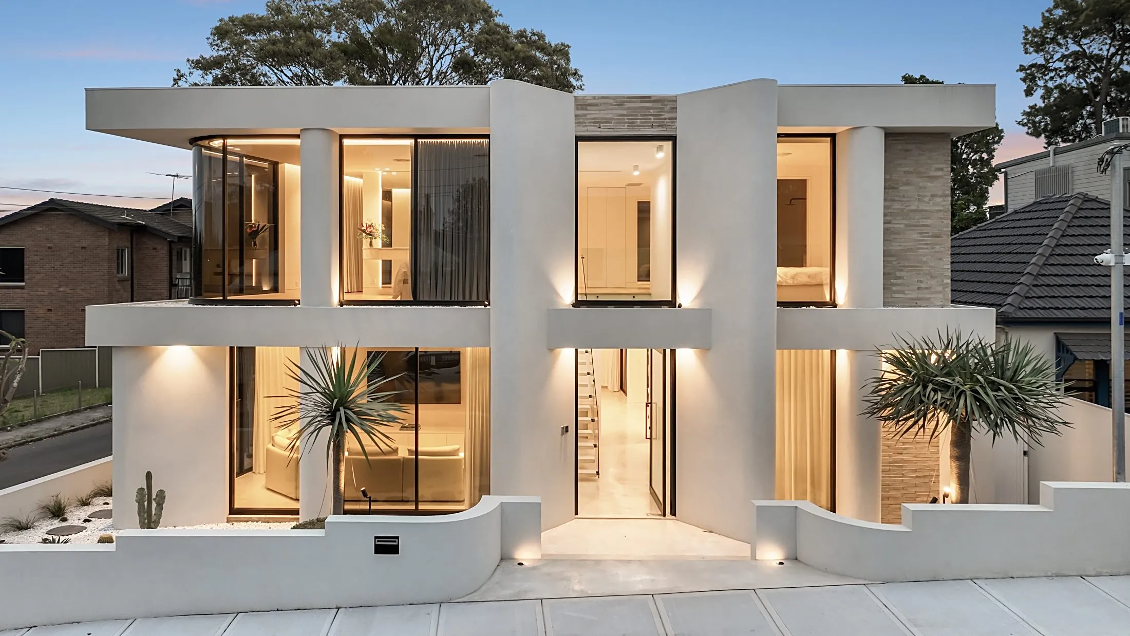 Two-storey rendered home at dusk with warmly lit windows, Lilyfield