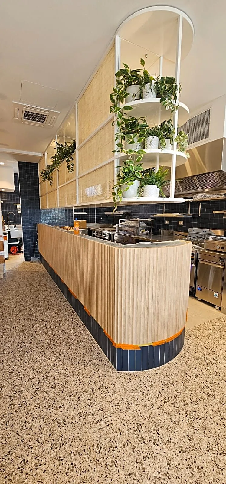 Restaurant counter with a timber fluted front and blue tile base beneath a white planter shelf, Rozelle